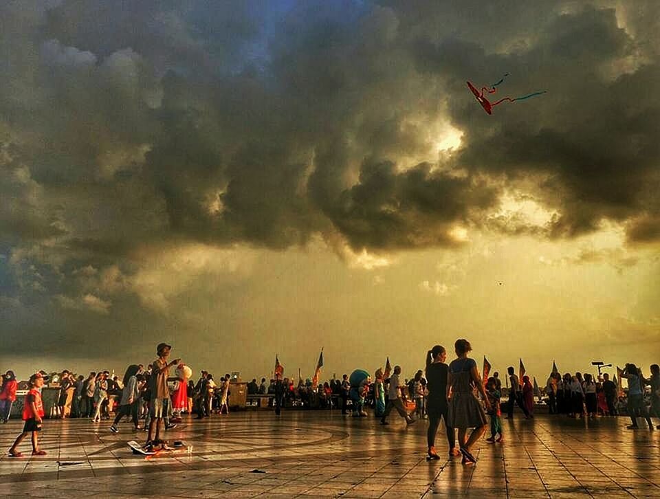 PEOPLE ON BEACH AGAINST CLOUDY SKY AT SUNSET