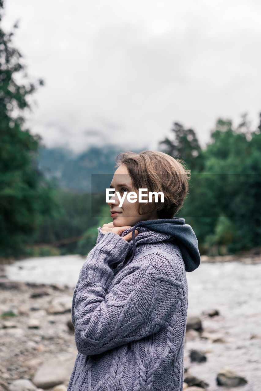 Young woman looking away while standing against trees in forest