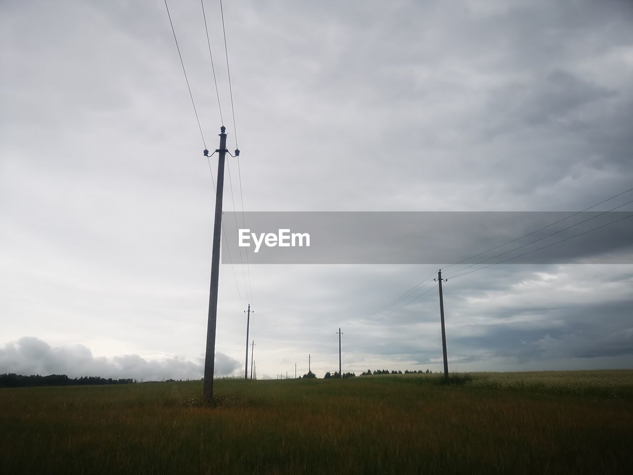 Silhouette electricity pylon on field against cloudy sky