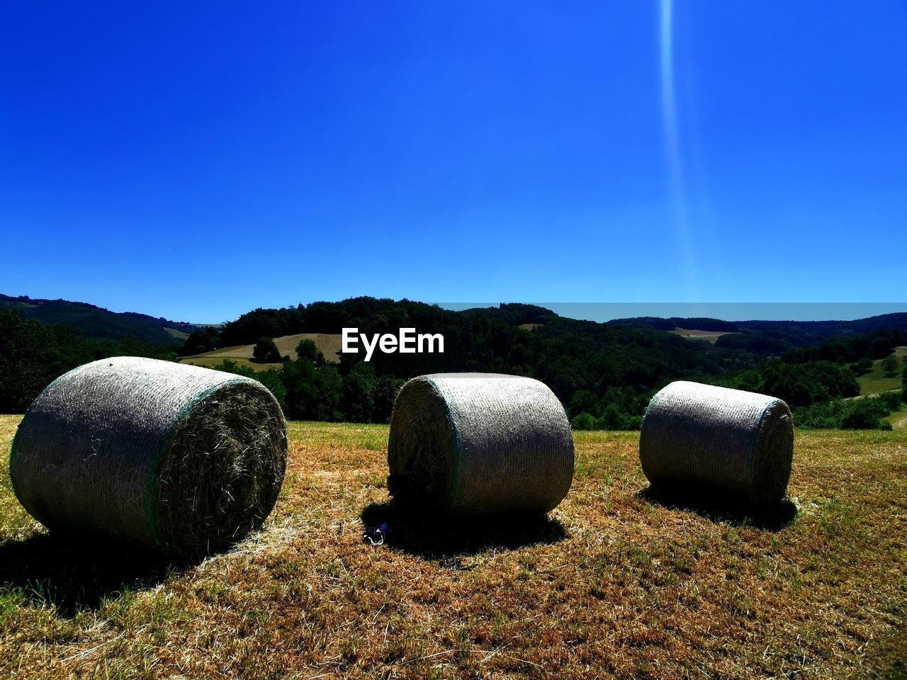 Hay bales on field against clear blue sky