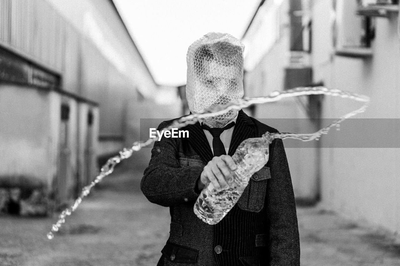 Man with a bottle of water on his hand and bubble wrap covering his face 