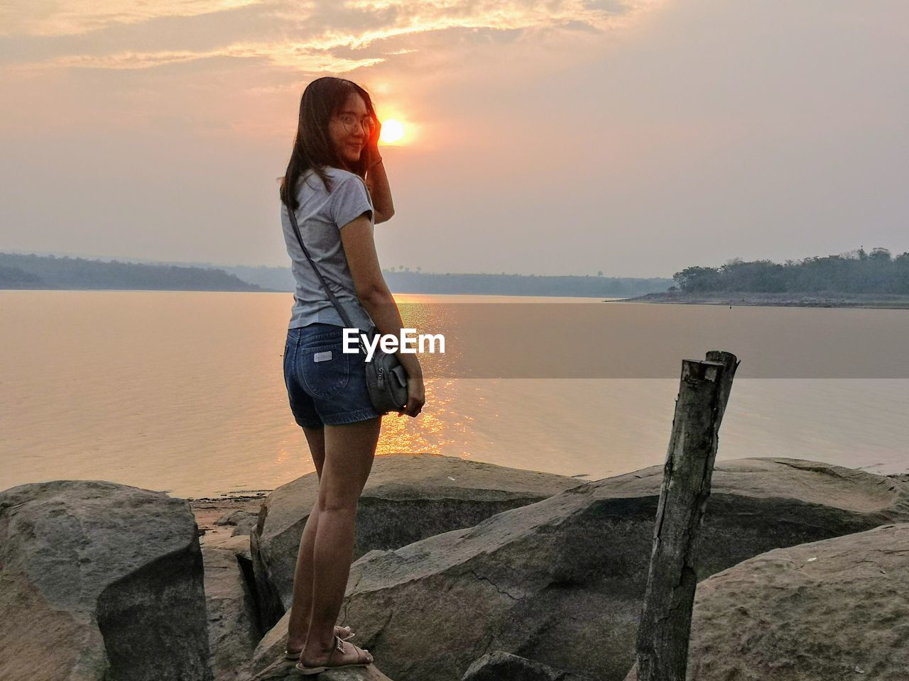 Woman standing on rock against sky during sunset