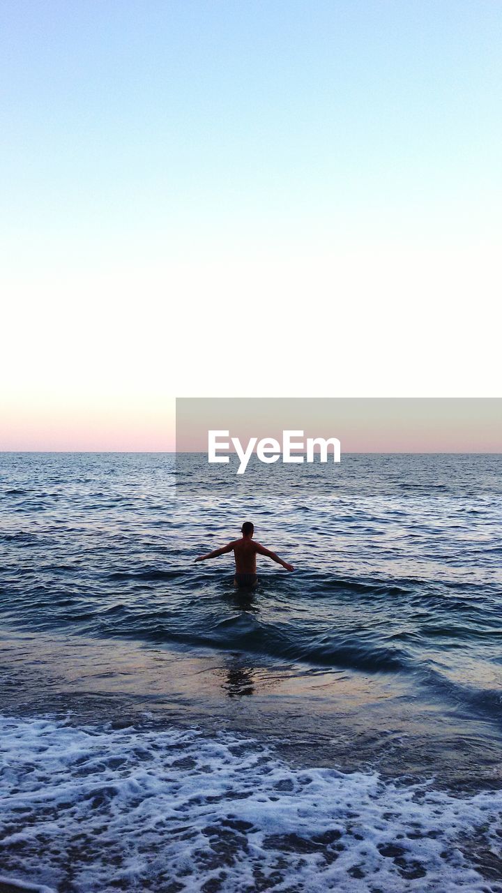 Rear view man standing in sea against sky during sunset