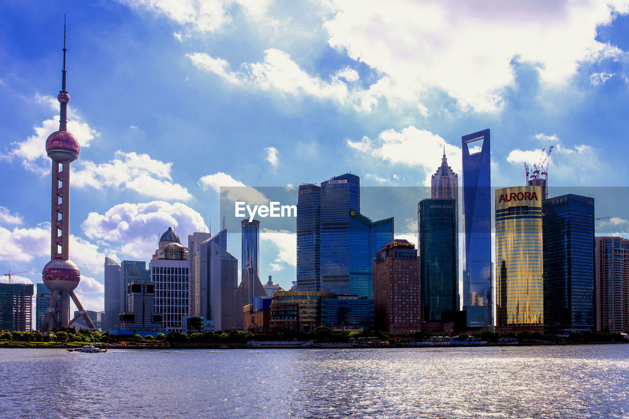 Modern buildings by huangpu river against cloudy sky