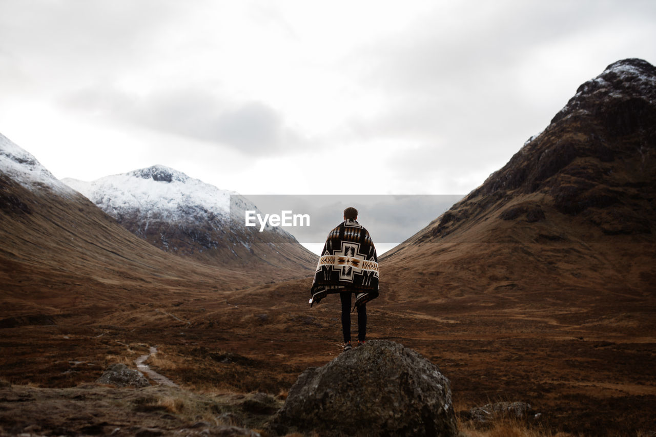 Back view of unrecognizable male explorer standing on rock and enjoying scenery of mountains in fall in scottish highlands