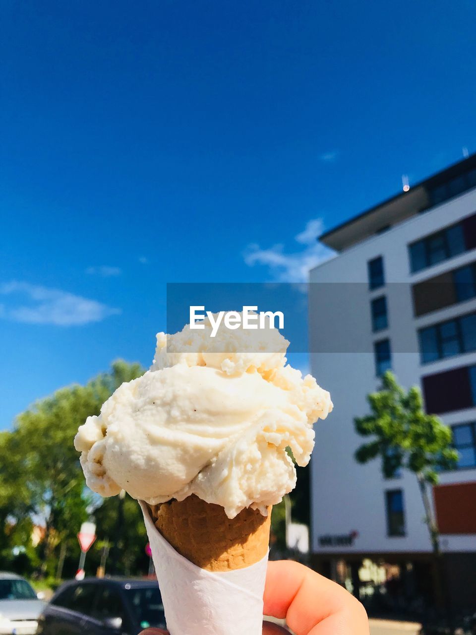 Cropped hand holding ice cream cone against blue sky