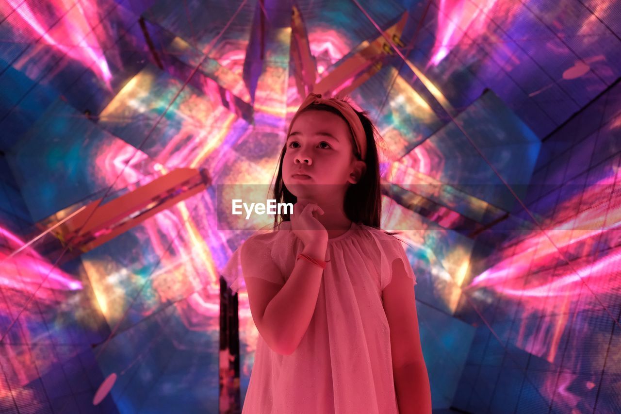 DIGITAL COMPOSITE IMAGE OF YOUNG WOMAN LOOKING AT ILLUMINATED NIGHTCLUB