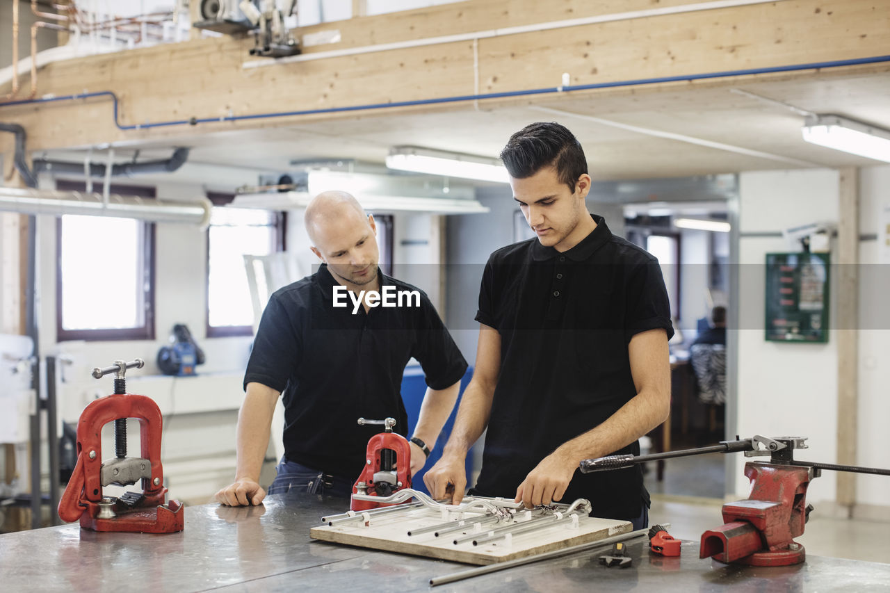 Auto mechanic teacher looking at male student working at workshop