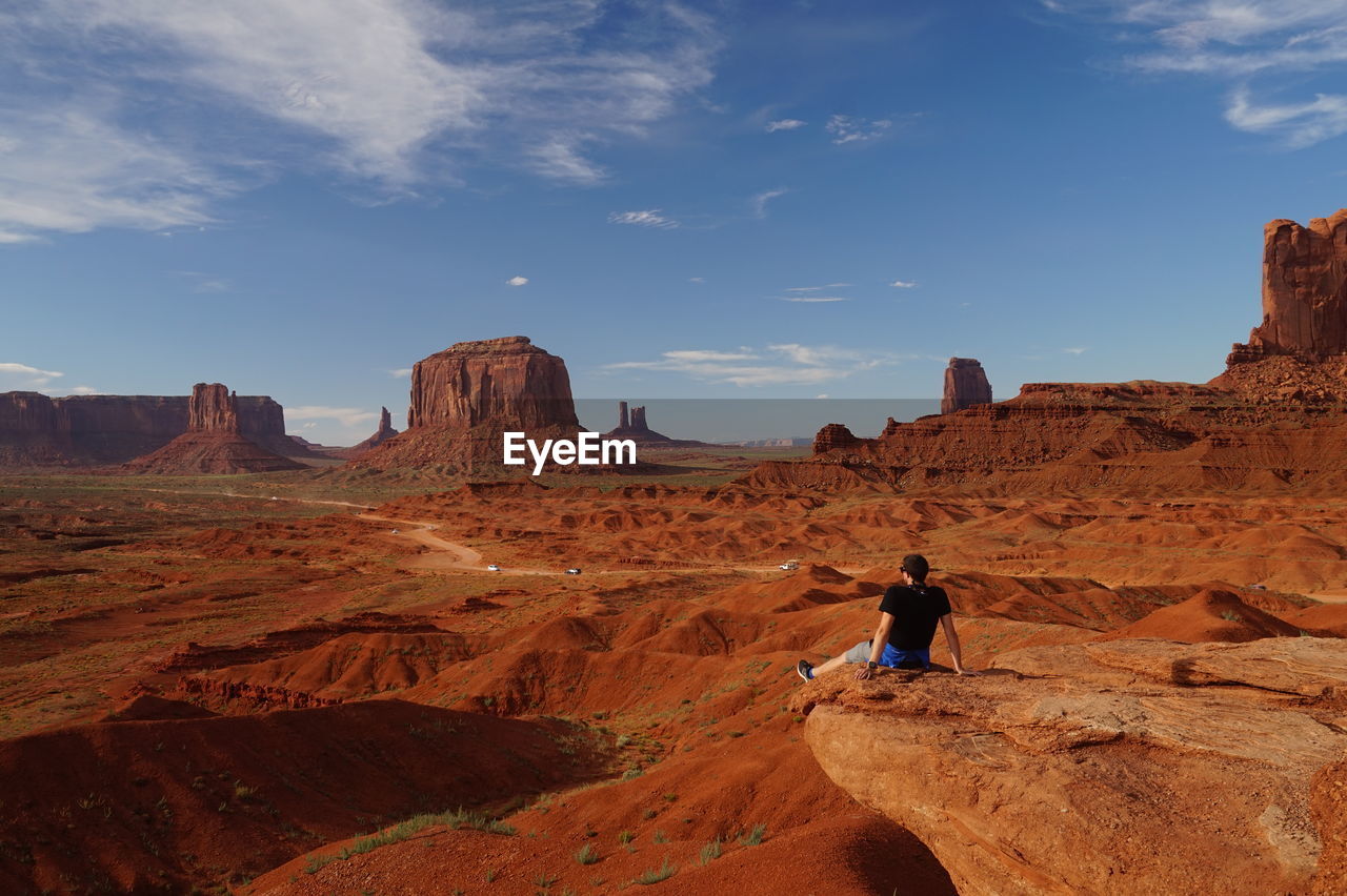 MAN STANDING ON ROCK FORMATION IN DESERT