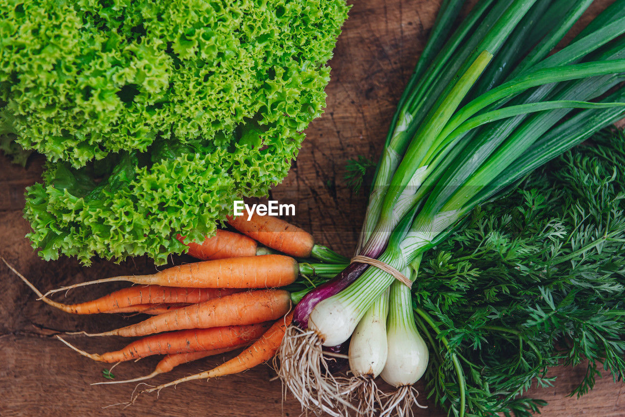 Orange carrots, green onions and lettuce on a wooden background. bunches of organic fresh vegetables