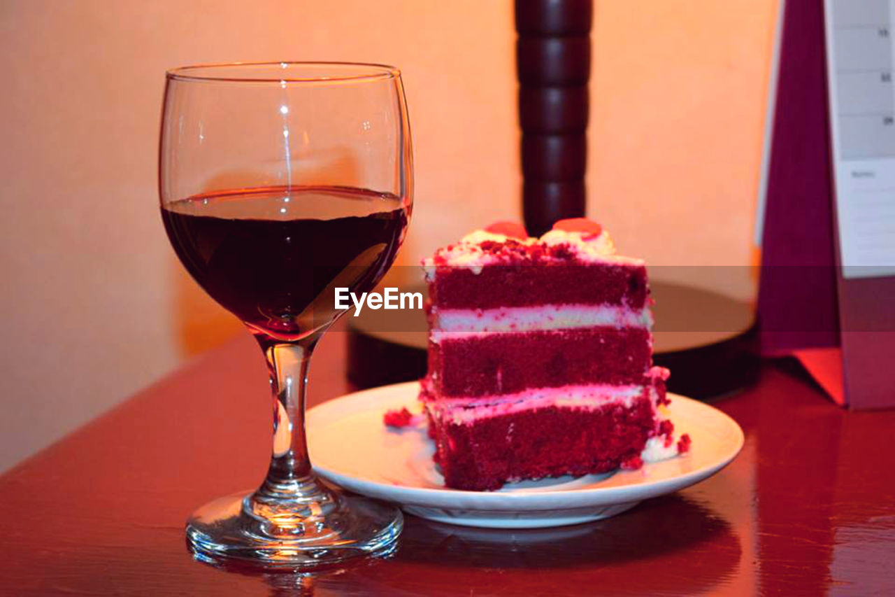 Wine with red velvet cake on table