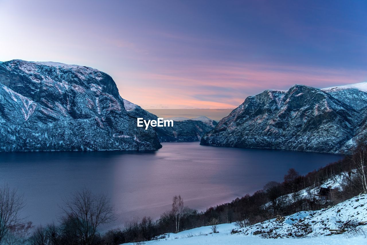 Scenic view of lake by snowcapped mountains against sky during sunset