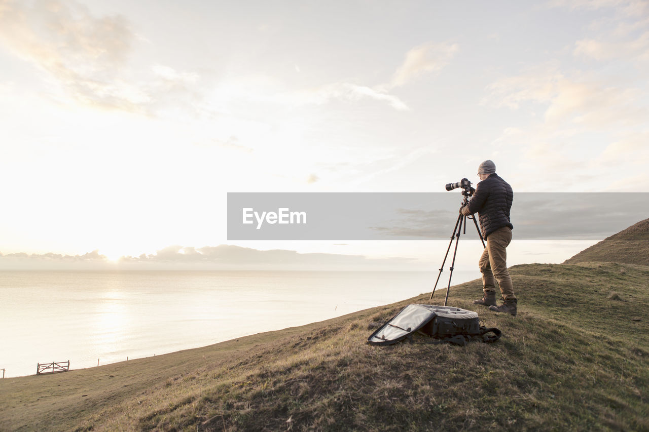 Rear view of hiker photographing sea through slr camera while standing on hill