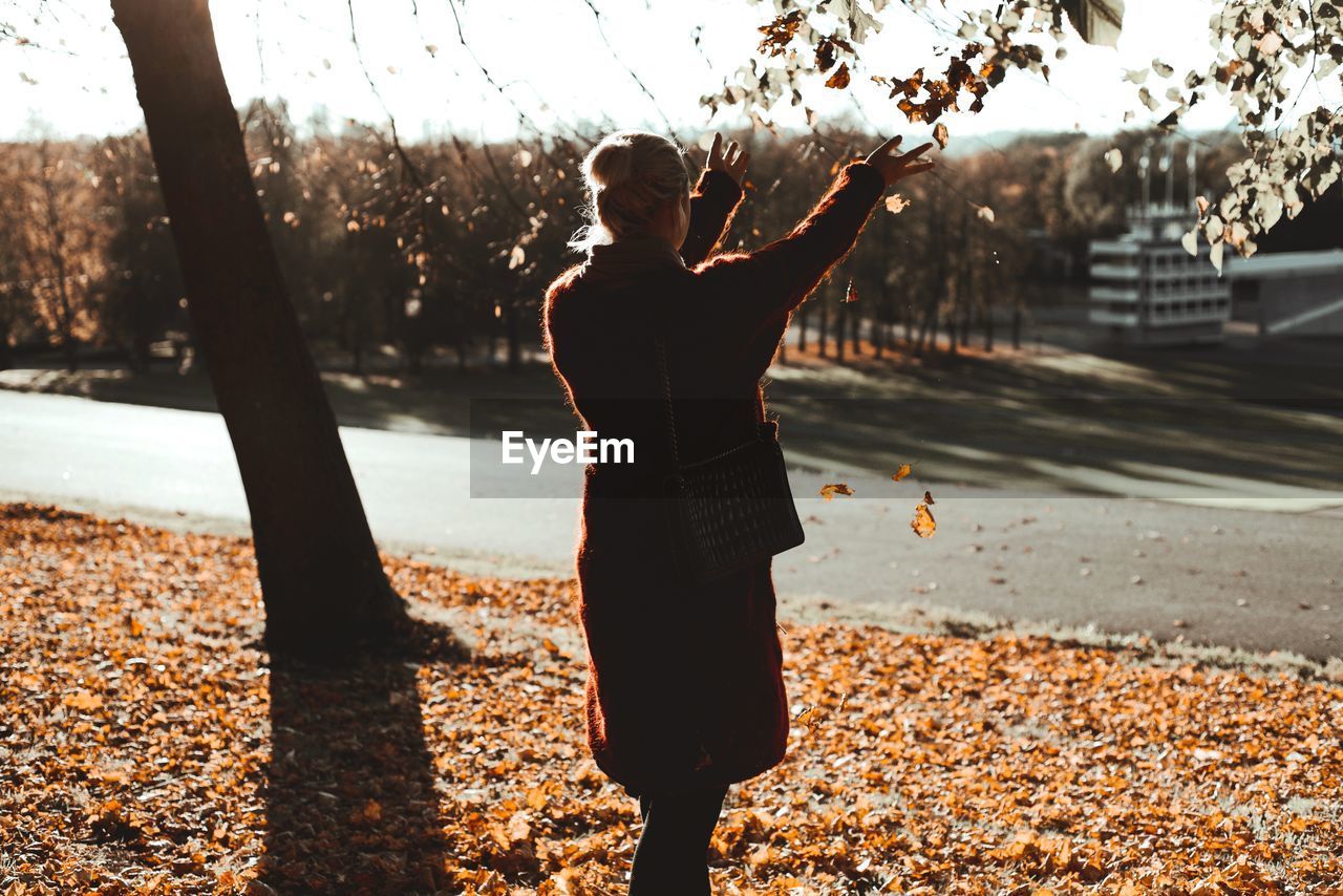 FULL LENGTH OF WOMAN STANDING ON TREE DURING AUTUMN