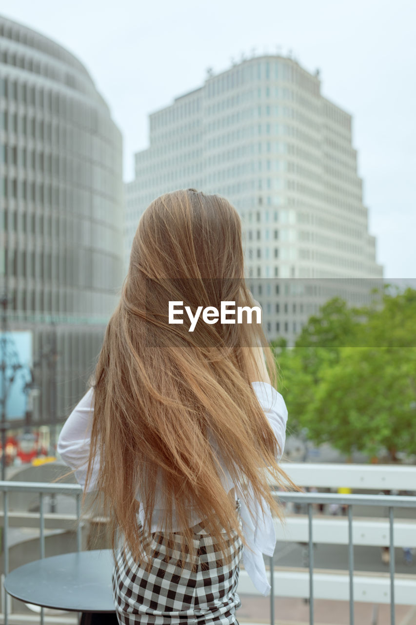 Rear view of young woman standing outdoors against sky