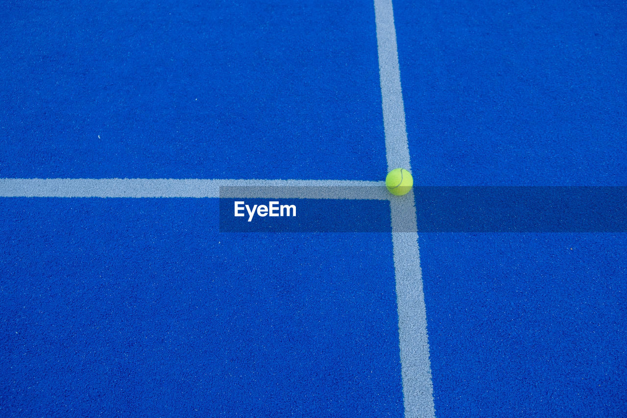 A ball on the line of a paddle tennis court of blue synthetic grass. health and sport concept
