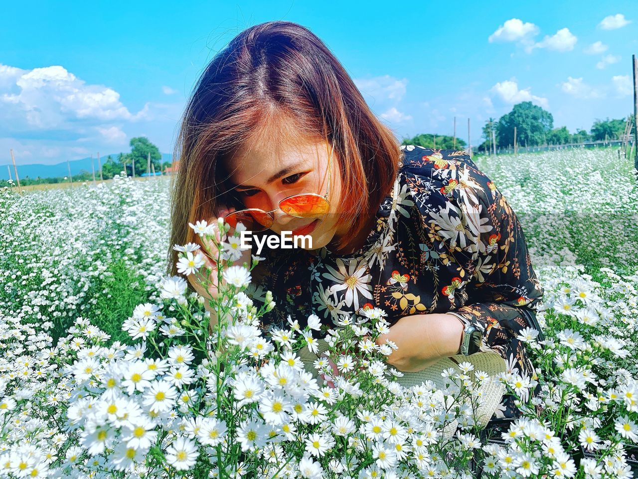 Woman wearing sunglasses looking at flowers growing on land