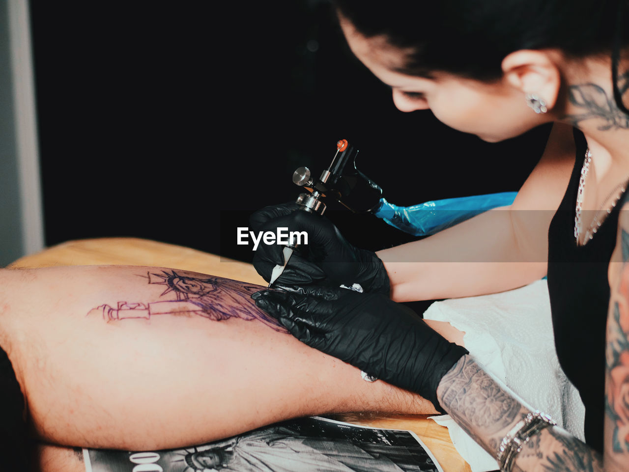 Young woman tattooing statue of liberty man on calf at parlor