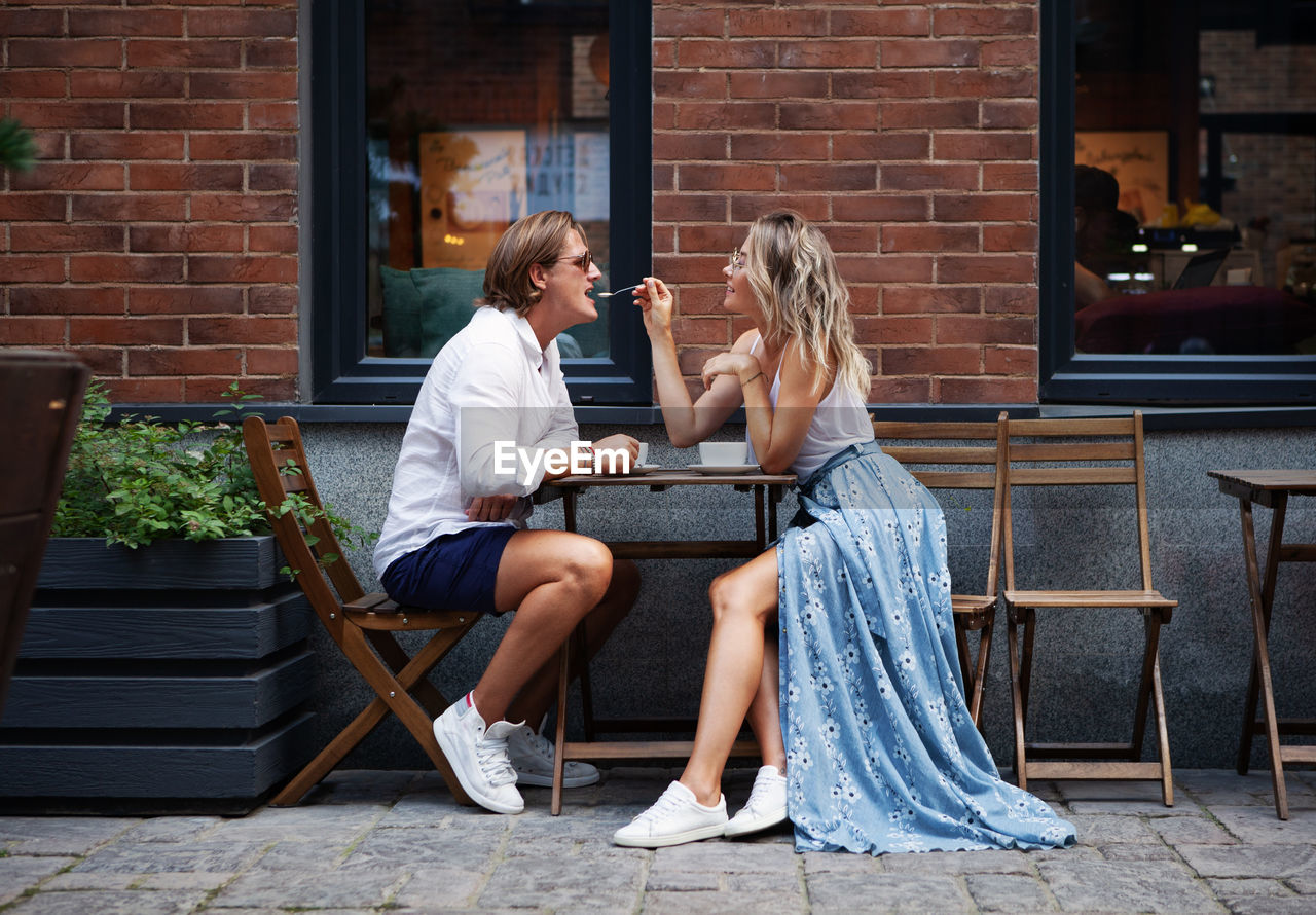 Fashionable  couple sitting in cafe and drinking coffee outside near. woman feeding  man