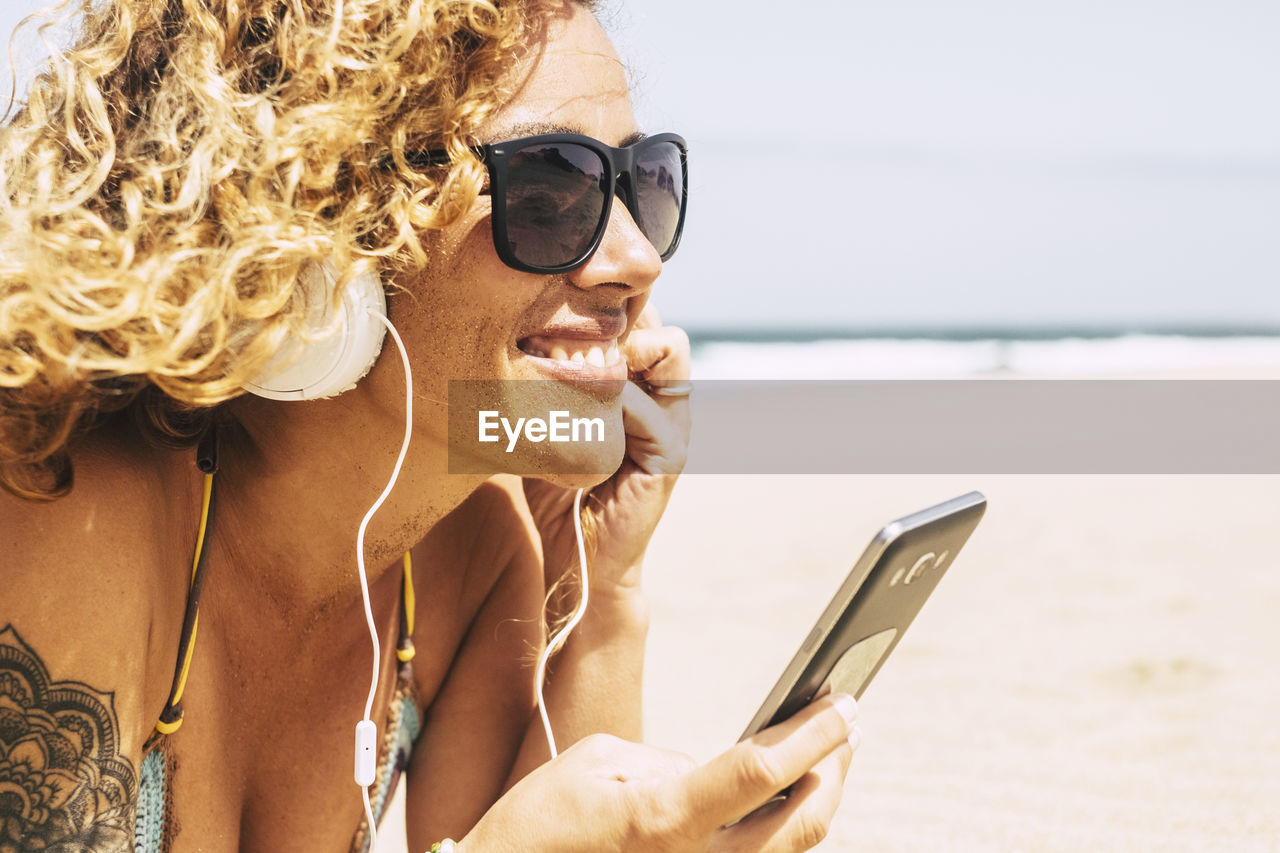 Smiling woman listening music while lying at beach during summer