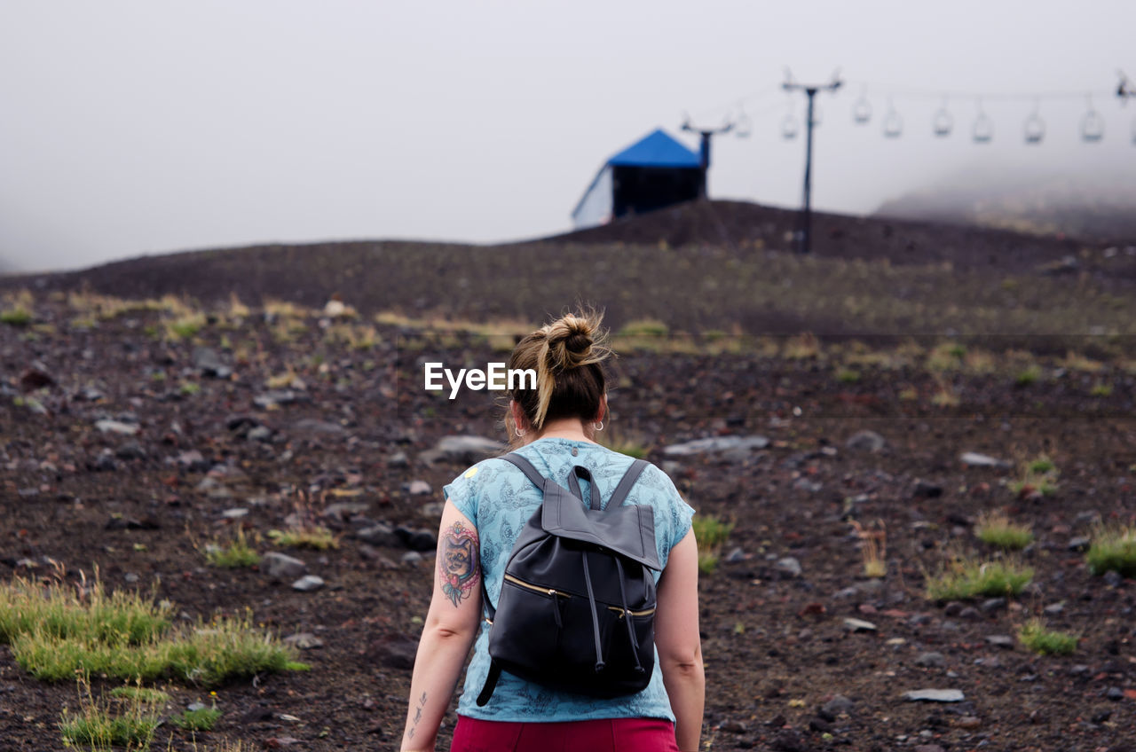 Rear view of female hiker walking on mountain against sky