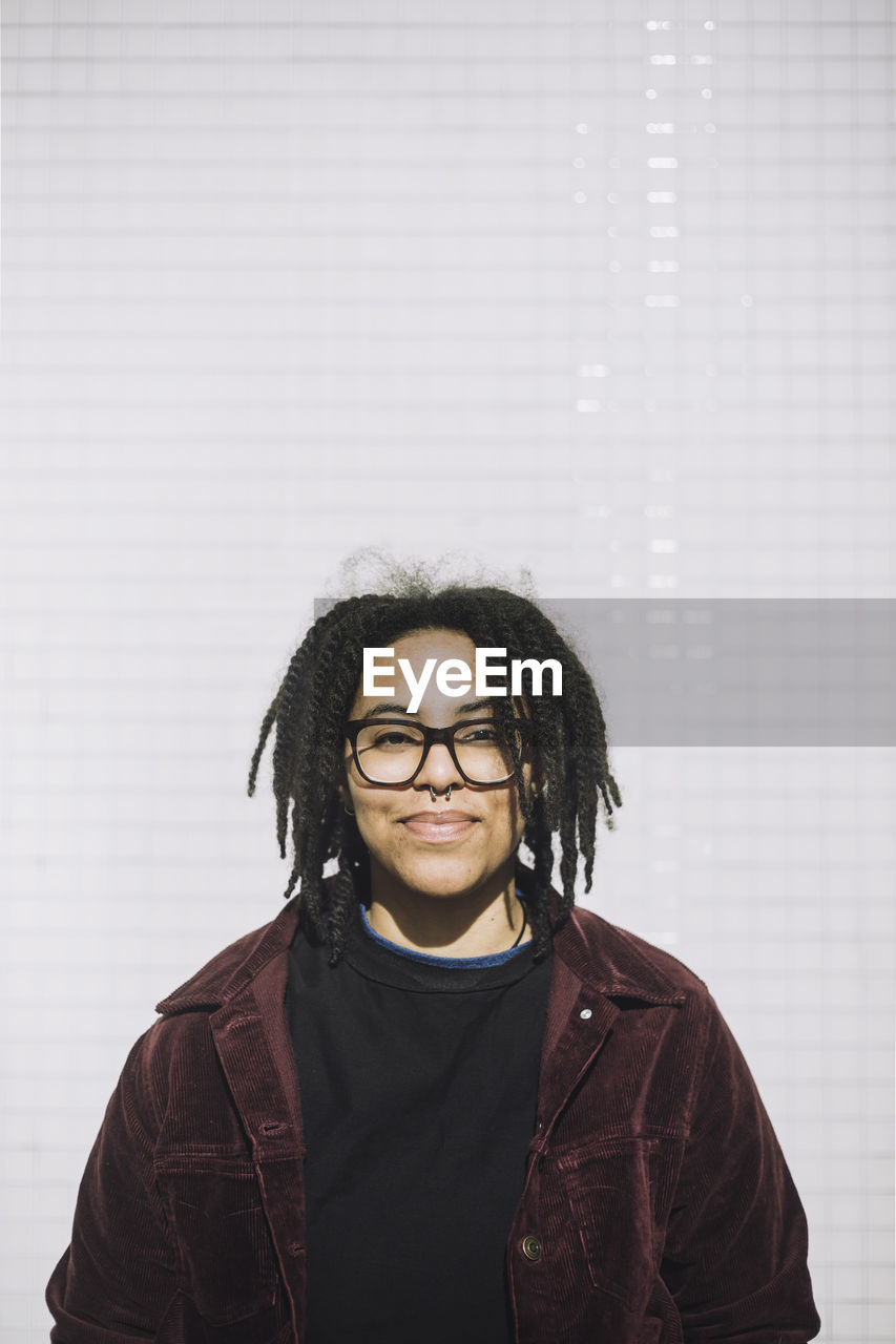 Portrait of smiling genderqueer person wearing eyeglasses standing against wall