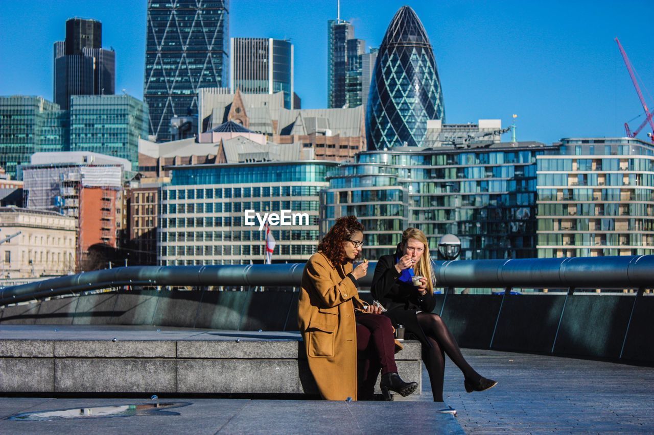 WOMAN SITTING ON MODERN BUILDINGS IN CITY