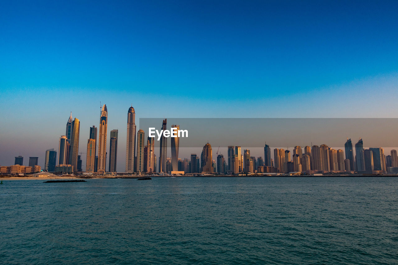 River by modern buildings against clear sky during sunset