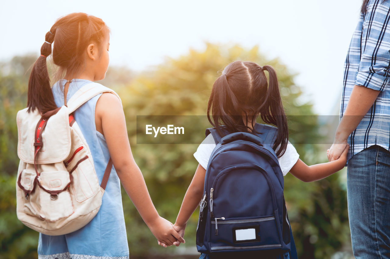 Rear view of girls with backpacks standing outdoors