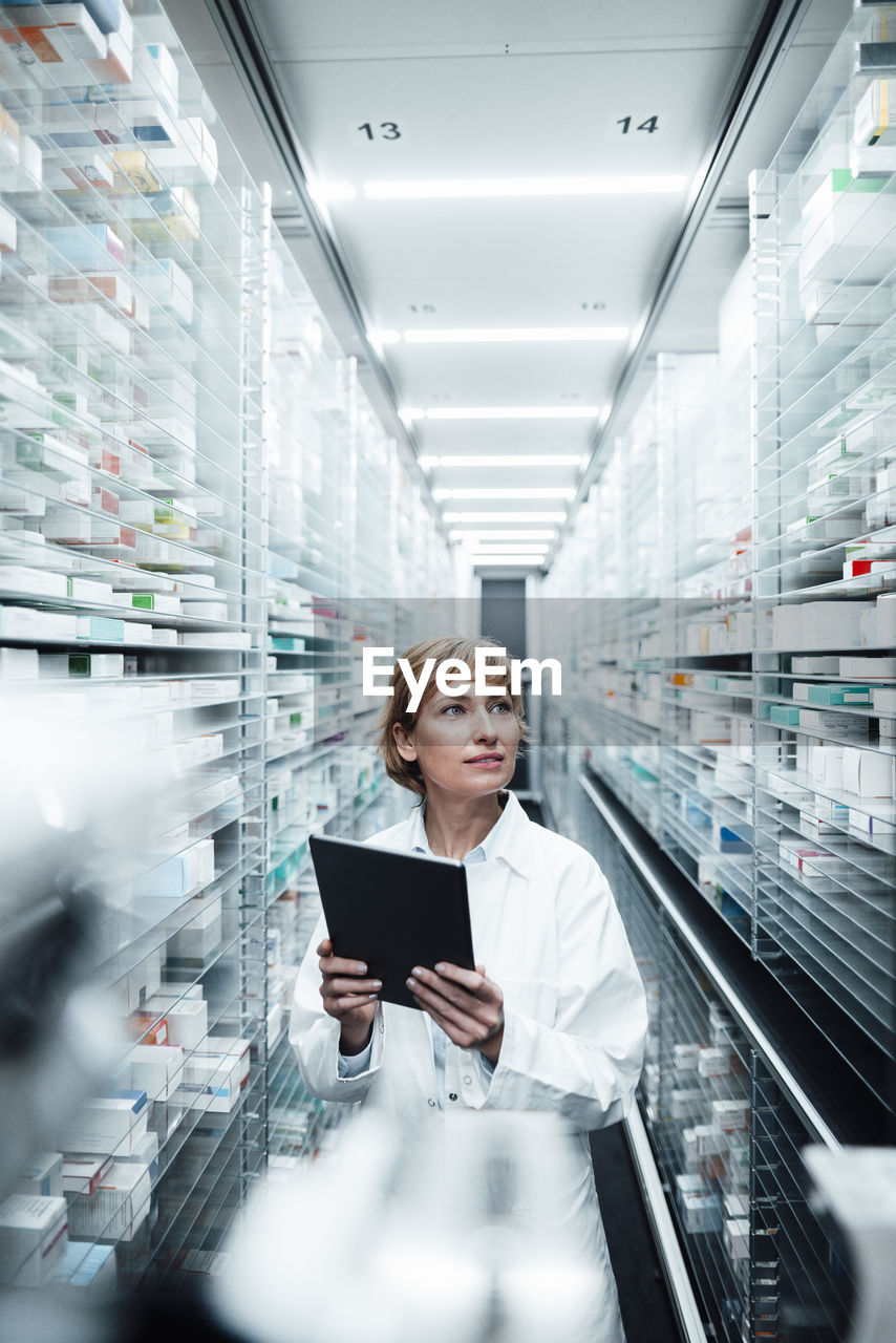 Female pharmacist holding digital tablet while searching medicine at medical store