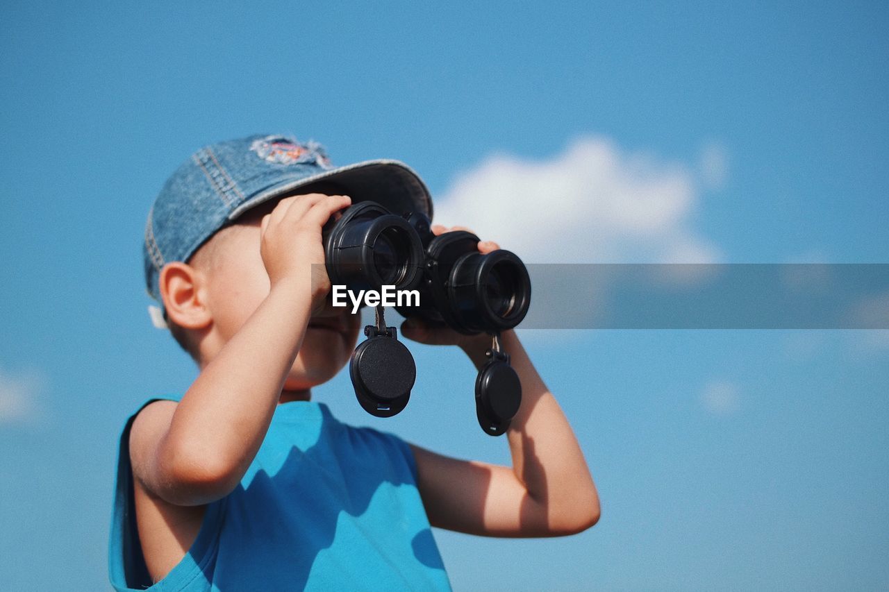 Low angle view of boy looking through binoculars while standing against sky