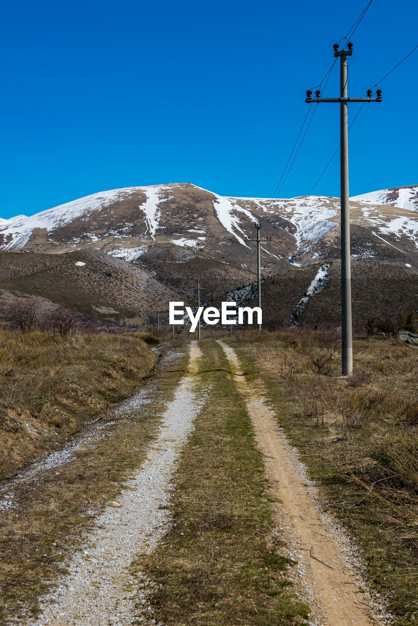 Road amidst snowcapped mountains against clear blue sky