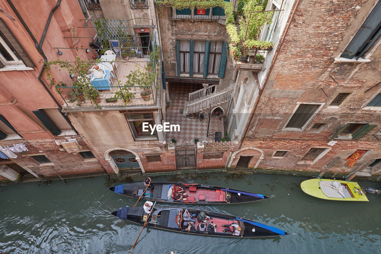 High angle view of people in gondolas on canal by buildings