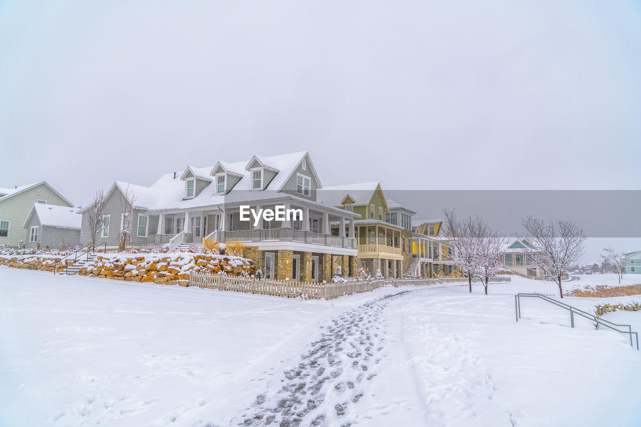 SNOW COVERED HOUSES BY BUILDING AGAINST SKY DURING WINTER