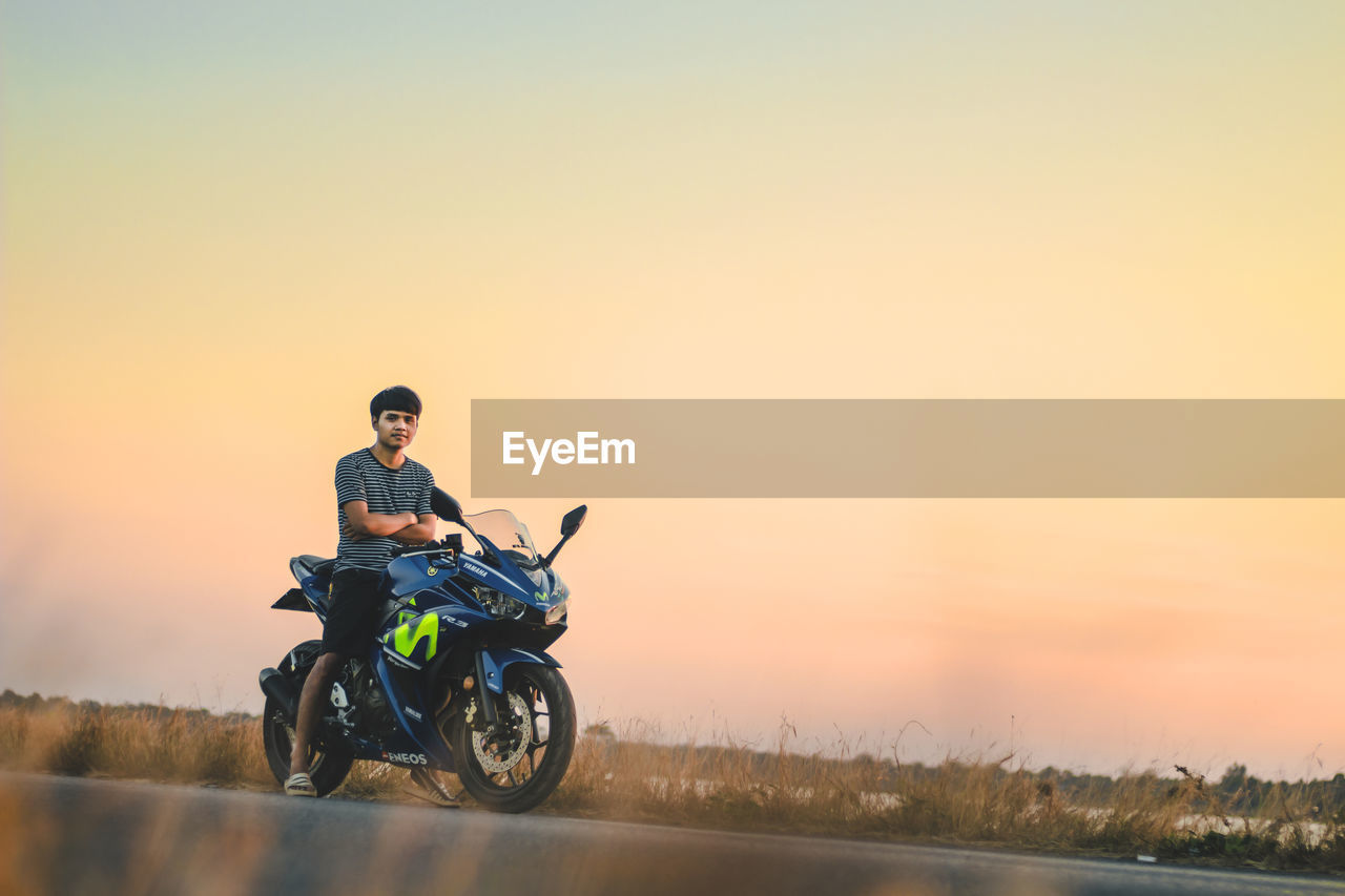 Portrait of man sitting on motorcycle at road against sky during sunset