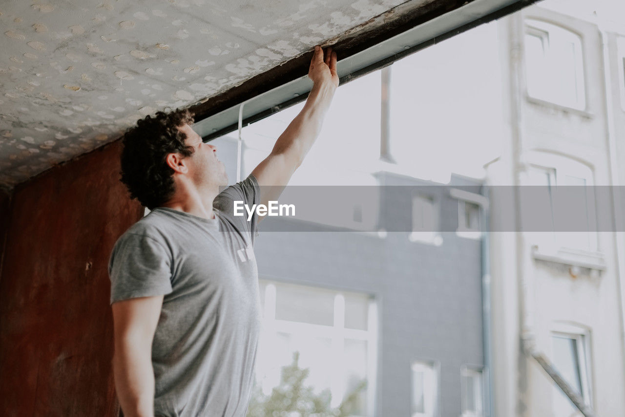 A young caucasian man repairing a window opening while and cleaning the frames with his hand