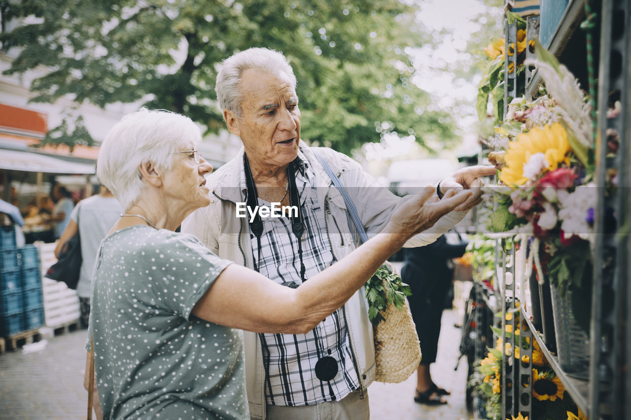 Retired couple discussing while shopping for flowers at market in city