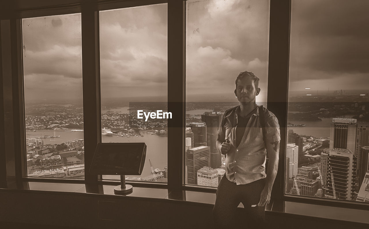 MAN LOOKING THROUGH WINDOW AT CITYSCAPE