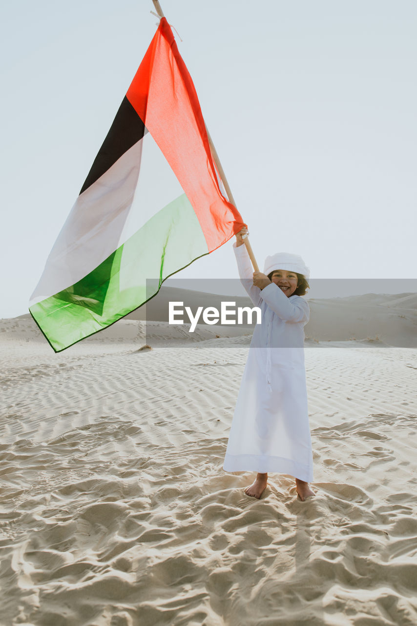 Portrait of happy standing on united arab emirates flag at desert