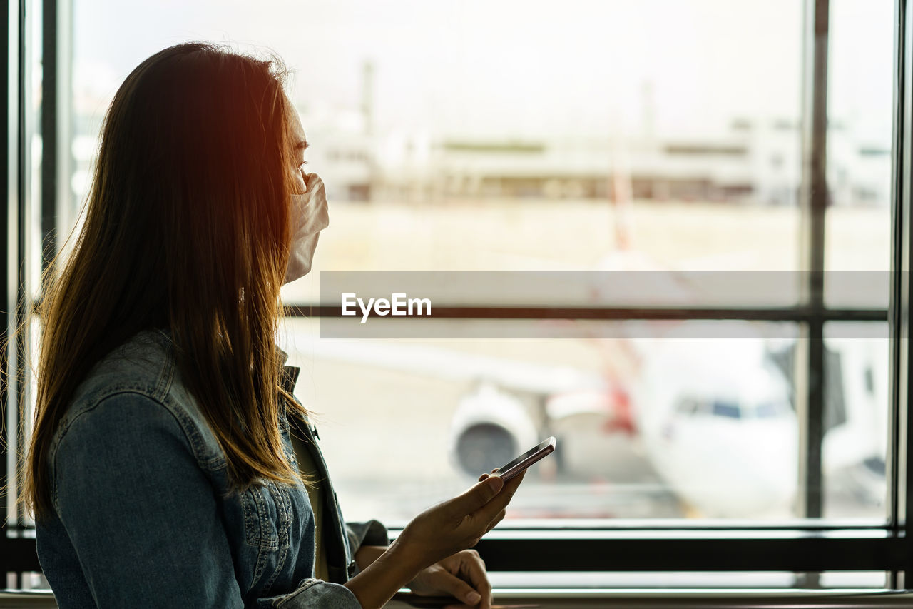 Side view of young woman using phone on window