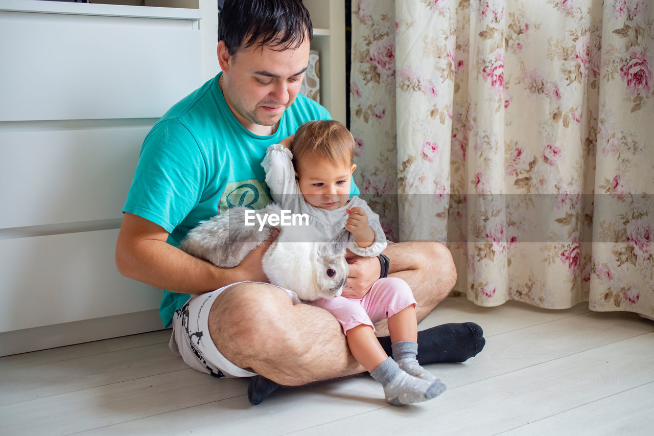 siblings playing with teddy bear while lying on floor at home