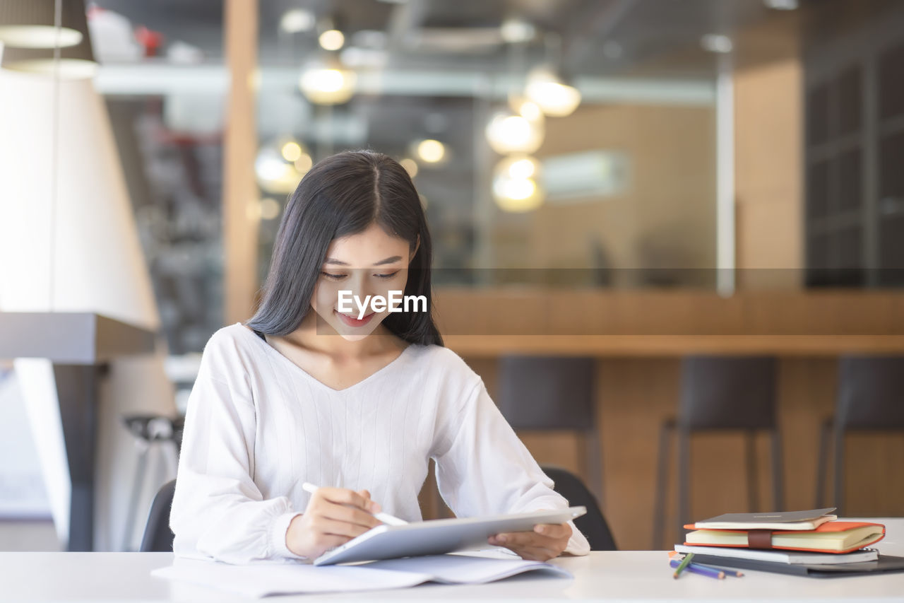 Young businesswoman using digital tablet while sitting at desk in office