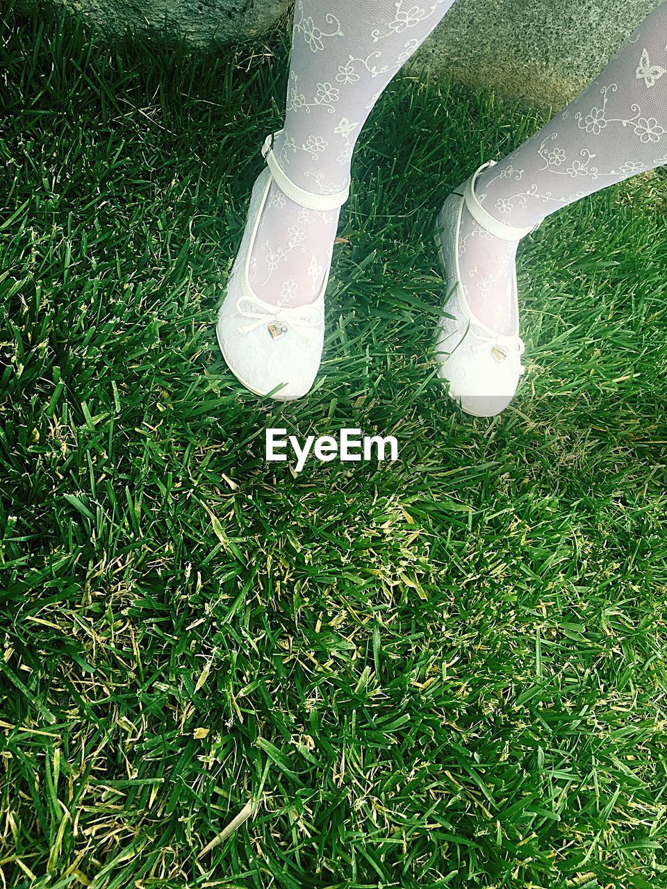 Low section of woman wearing white shoes while standing on grassy field