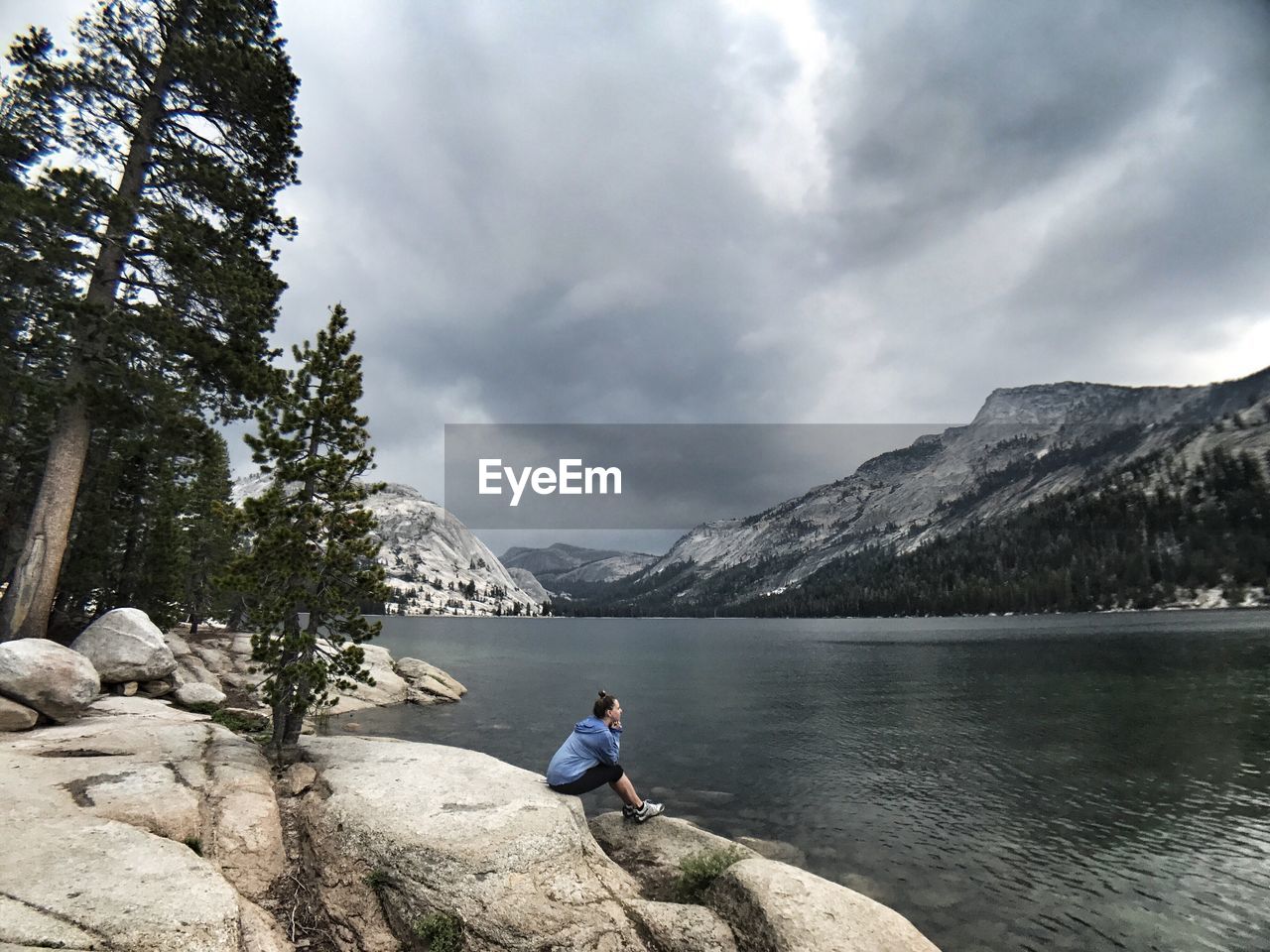 Side view of woman sitting by lake against mountains