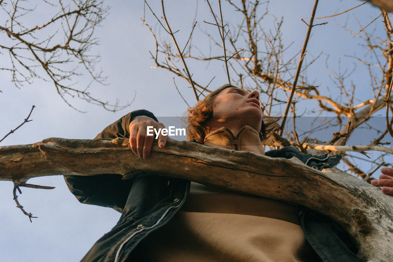 LOW ANGLE VIEW OF MAN ON TREE AGAINST SKY