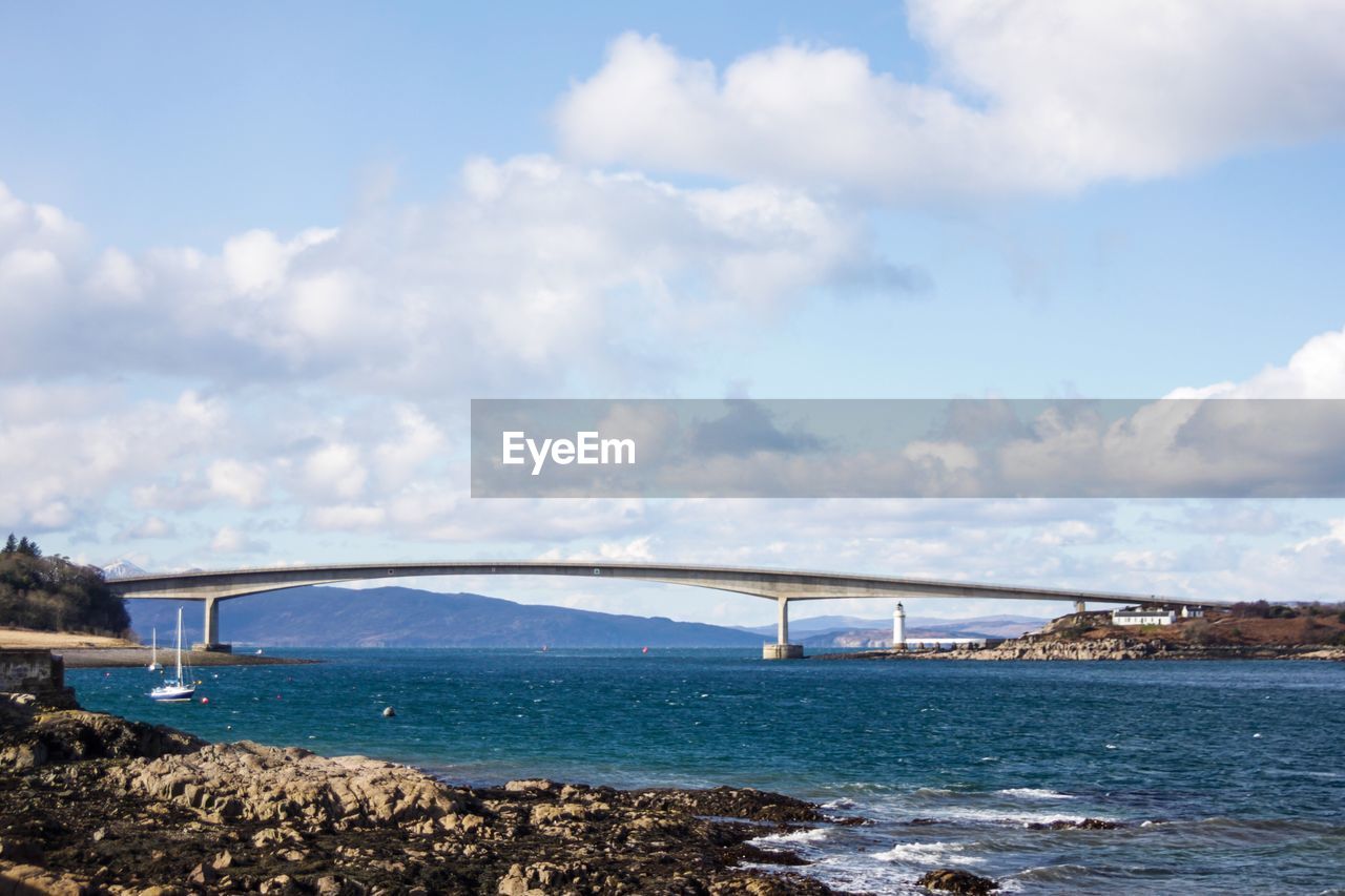 Bridge over sea against cloudy sky