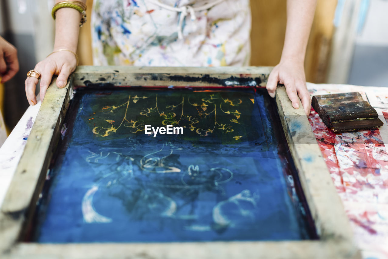 Crop woman placing silkscreen on textile before pouring ink