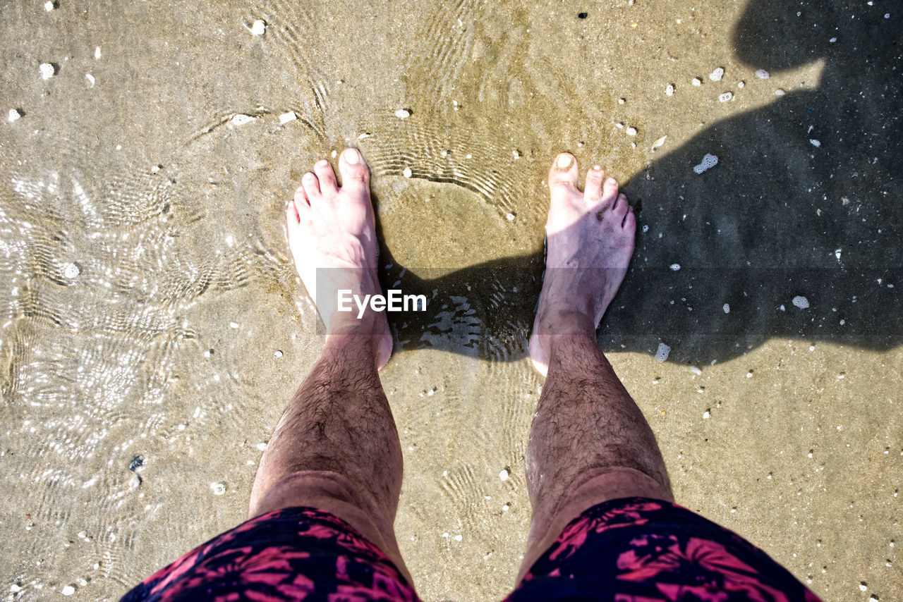 LOW SECTION OF PERSON STANDING ON SAND