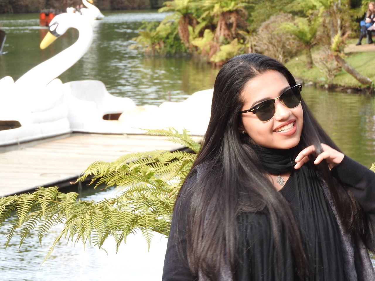 Happy woman with hand in hair standing by lake in park