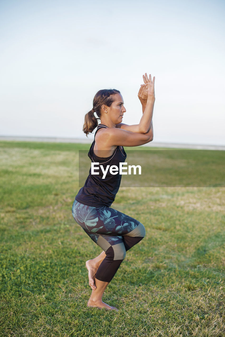 Mature woman exercising on field against sky